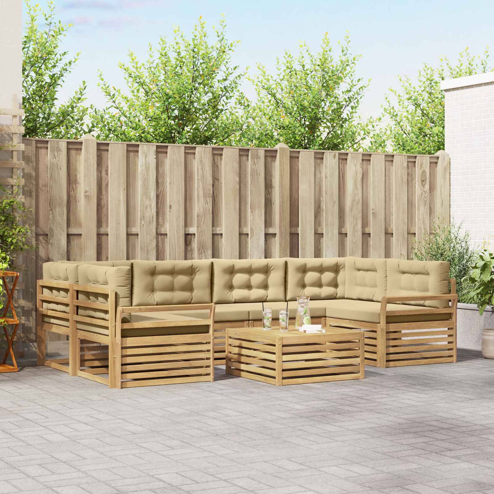 Gartenmöbel-Sitzsatzgruppe mit beigefarbenen Kissen und Holzrahmen mit Lamellenkonstruktion um einen niedrigen Couchtisch auf einer gefliesten Terrasse neben einem Holzzaun.