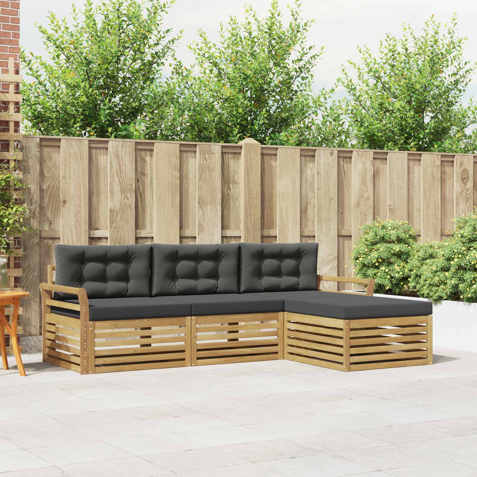 Outdoor-Lounge-Sofa mit schwarzen Kissen und Holzlatten-Rahmen auf einer gepflasterten Terrasse neben einem Zaun und Sträuchern.