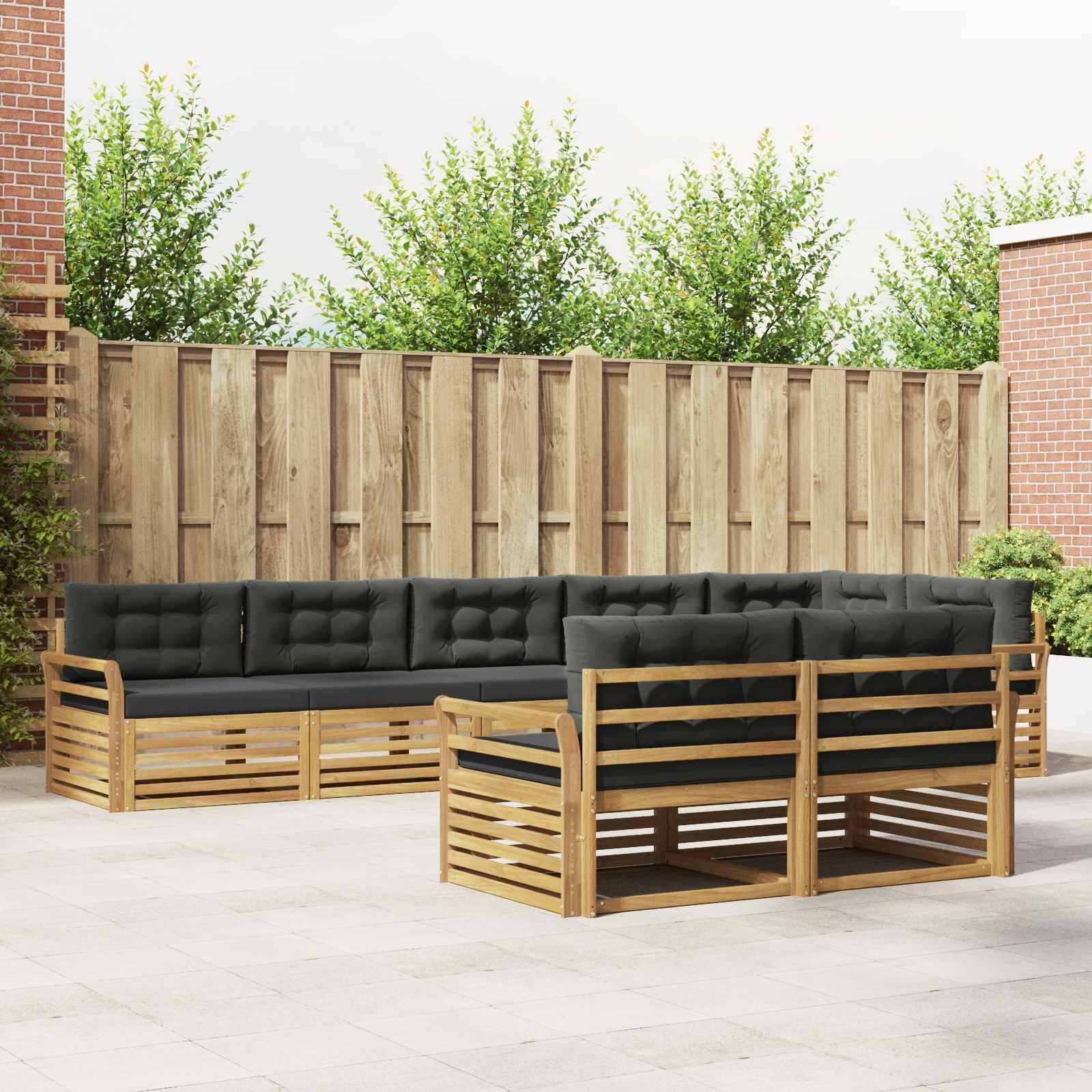 Outdoor-Terrassenmöbel-Set mit schwarzen gepolsterten Holzsofare und Sesseln, die um einen niedrigenTisch in einem eingezäunten Gartenhof angeordnet sind.