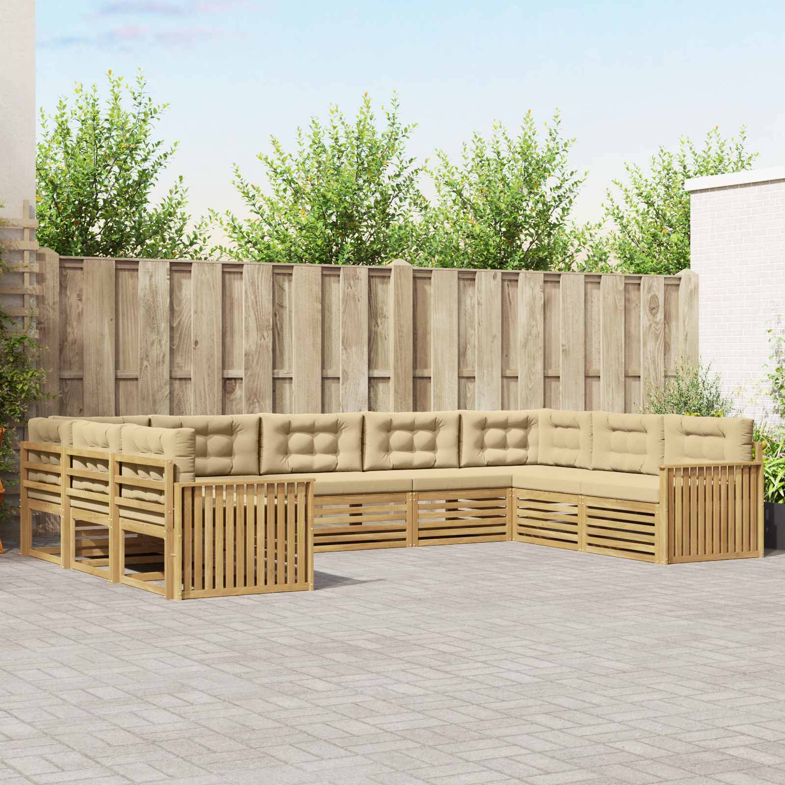 Außenterrasse mit einem L-förmigen Holz-Ecksofa und beigen Kissen an einem Holzzaun auf einer gepflasterten Terrasse mit Bäumen dahinter.
