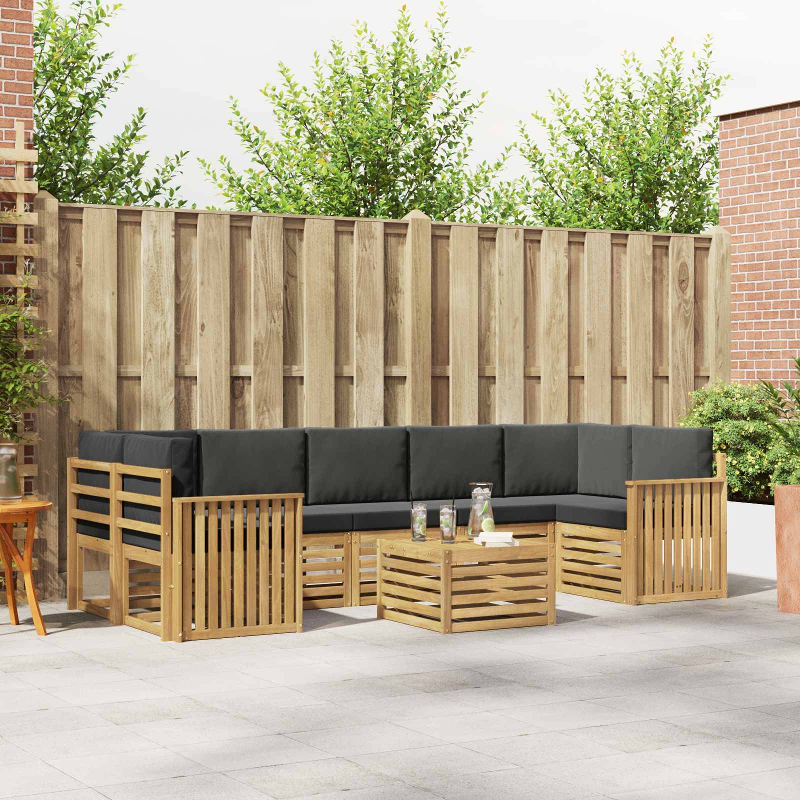 Außenbereich einer Terrasse mit schwarzen Kissen ausgestattetes Holz-Ecksofa, passender Tisch und Holztrennwand an einem Zaun.