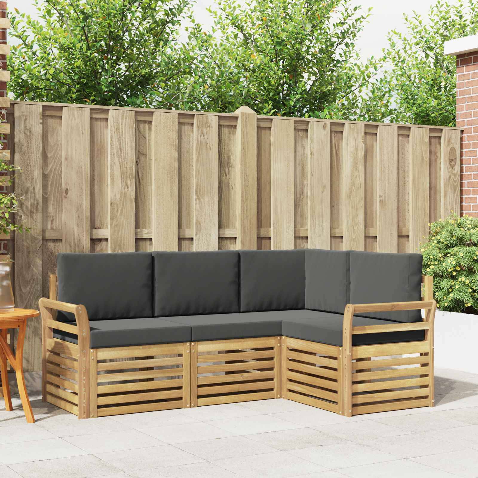 Outdoor-Ecksofa mit schwarzen Kissen und Holzlattenrahmen auf einer Terrasse, vor einem hohen Zaun und Grünflächen.