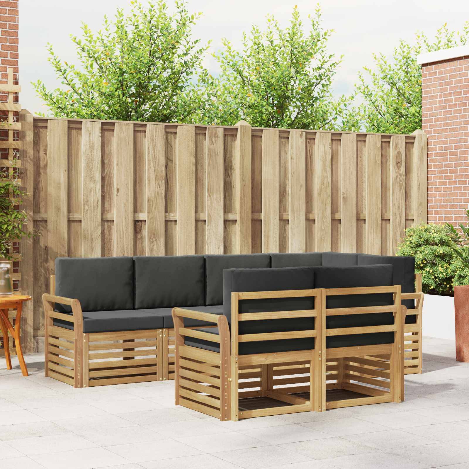 Outdoor-Terrassenmöbel-Set mit Holzrahmen und schwarzen Kissen, angeordnet um ein Ecksofa und zwei Sessel in einem eingezäunten Hof.