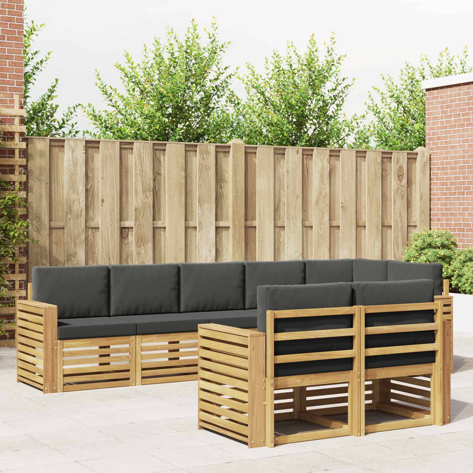 Terrasse im Freien mit zwei passenden Holz-Eckgarnituren und schwarzen Kissen, die um eine Ecke auf einer gepflasterten Terrasse neben einem Holzzaun und Ziegelmauern angeordnet sind.