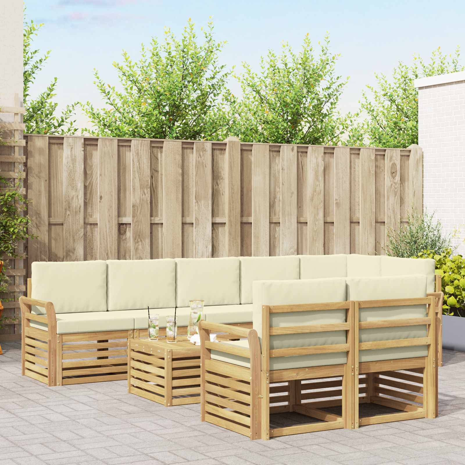 Outdoor-Terrassenmöbelset mit cremefarbenen Kissen und Holzrahmen, angeordnet um einen niedrigen Couchtisch in einem eingezäunten Hinterhof.