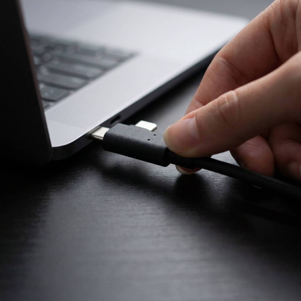 Eine Hand steckt ein USB-C-Kabel in einen Laptop-Anschluss auf einem Schreibtisch.