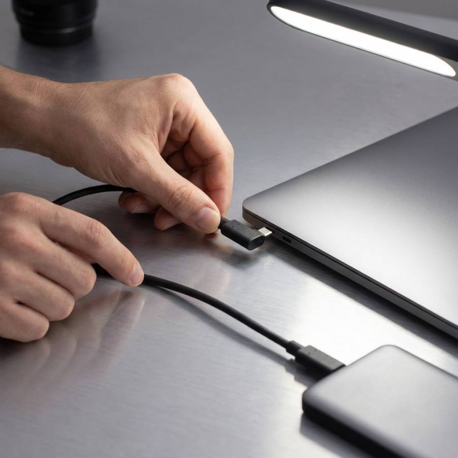Hände stecken ein USB-C-Kabel in einen Laptop neben einem externen Laufwerk auf einem Schreibtisch.