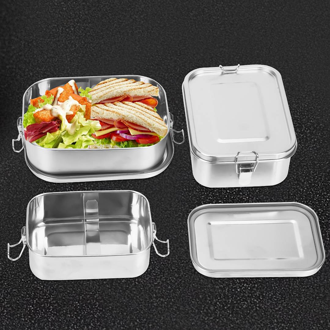 Vier Edelstahl-Lunchboxen auf dunklem Hintergrund; eine ist offen und mit Sandwiches und Salat gefüllt, drei sind geschlossen oder leer.