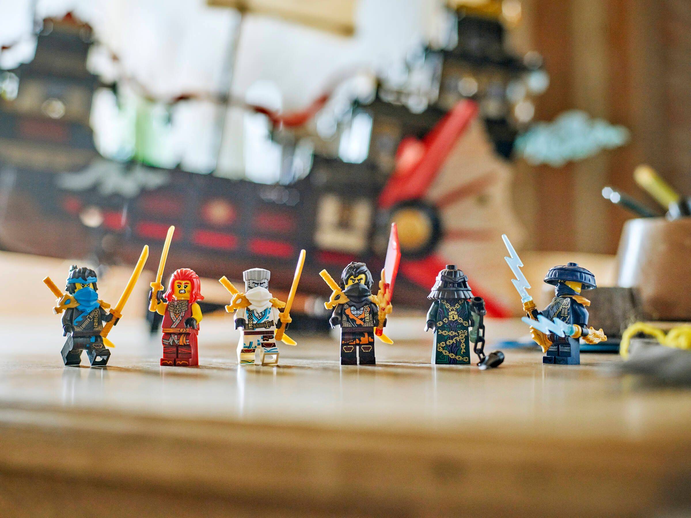 Sechs LEGO-Minifiguren stehen in einer Reihe auf einer Tischplatte, jede mit einer Waffe in der Hand, mit unscharfem Spielzimmerhintergrund.