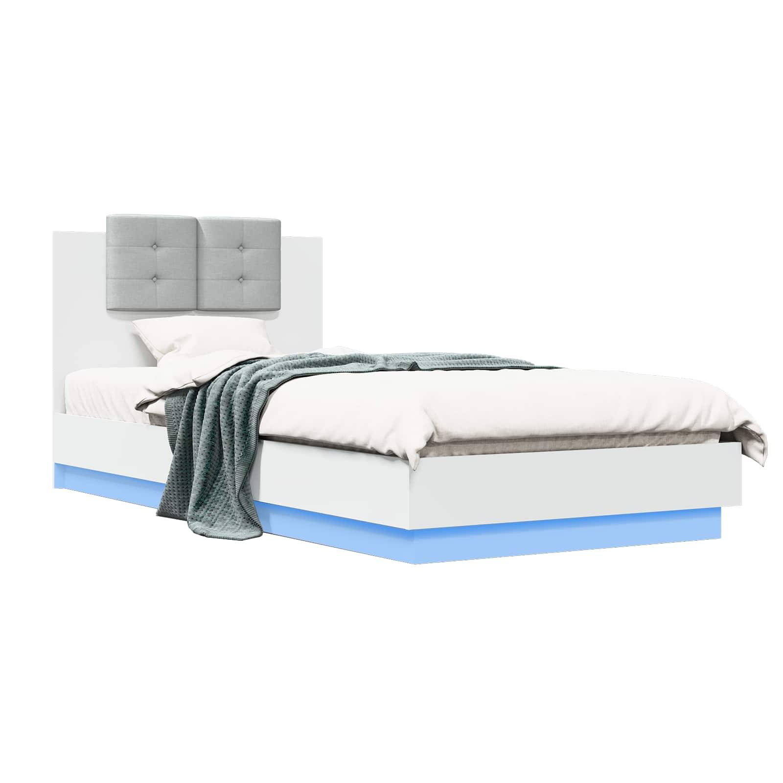 Modernes weißes Bett mit grauem gestepptem Kopfteil, weißer Bettwäsche und einer gefalteten blaugrünen Decke auf einem blau beleuchteten Sockel vor einem schlichten Hintergrund.