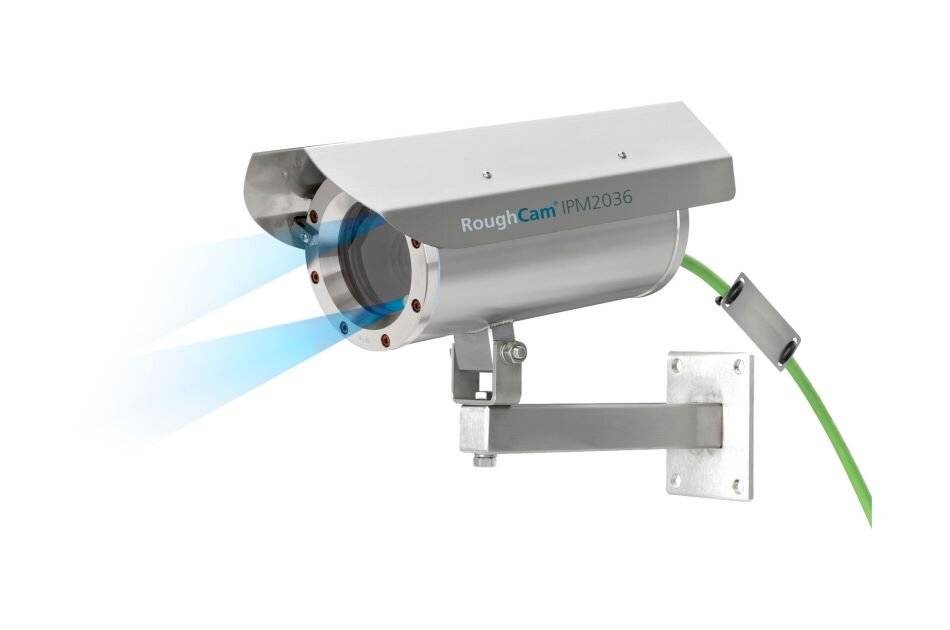 Silver RoughCam IPM2036 Industrie-Sicherheitskamera auf einer Wandhalterung montiert, mit grünem Kabel angeschlossen und blauen Erkennungsstrahlen, die nach vorne projizieren.