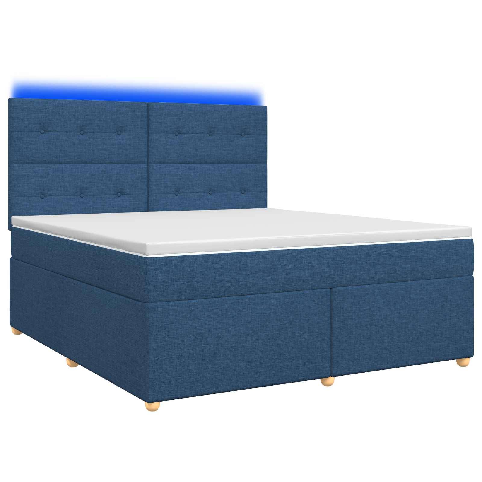 Bett mit blauem Polsterbezug, hohem gestepptem Kopfteil und weißer Matratze auf Boxspringrahmen.