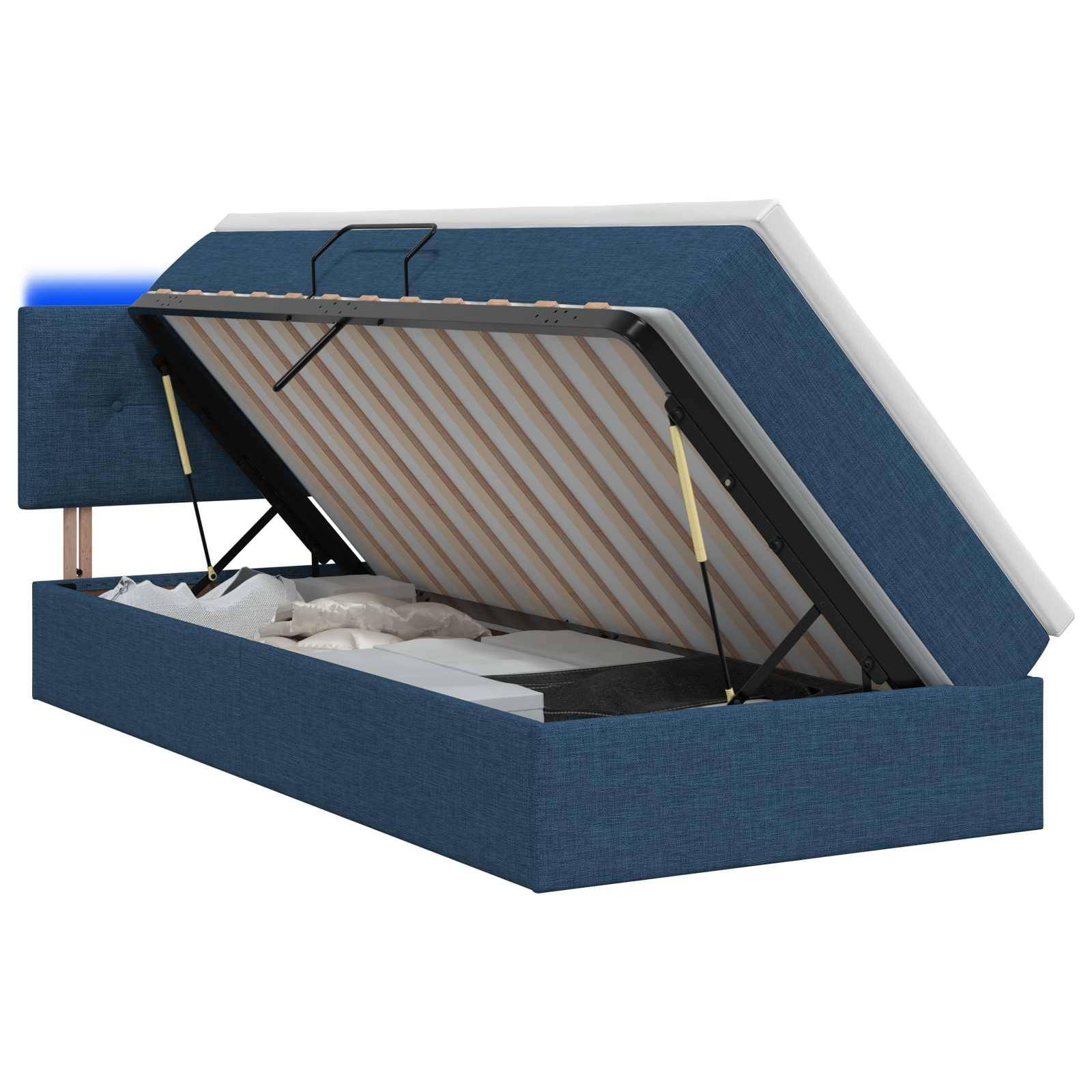 Blau gepolstertes Speicherbett mit angehobener Matratze auf einem Scharnierrahmen, das den Stauraum unter dem Bett freilegt.