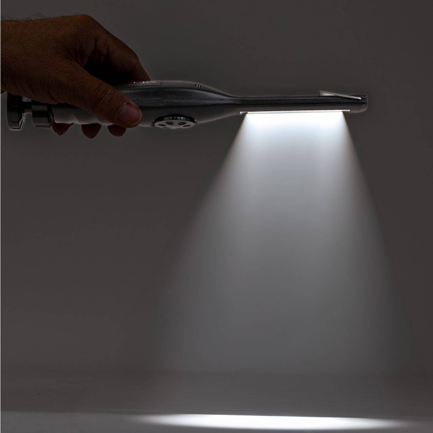 Eine Hand, die ein taschenlampenähnliches Gerät hält, das einen hellen Lichtkegel auf eine dunkle Oberfläche ausstrahlt und einen Scheinwerferkegel erzeugt.