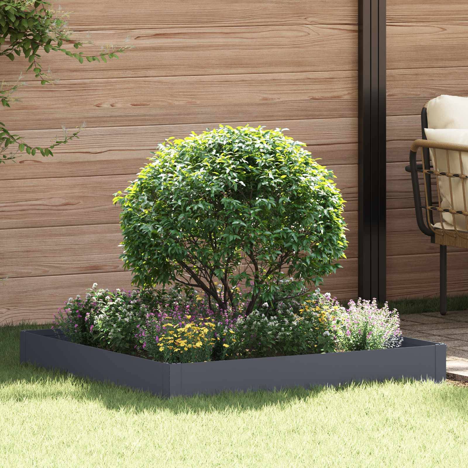 Ein kleines bepflanztes Blumenbeet mit einem rundgeformten Strauch und Blütenpflanzen in einem dunkel gefärbten rechteckigen Blumenkübel neben einer Holzwand und einem Terrassenstuhl.