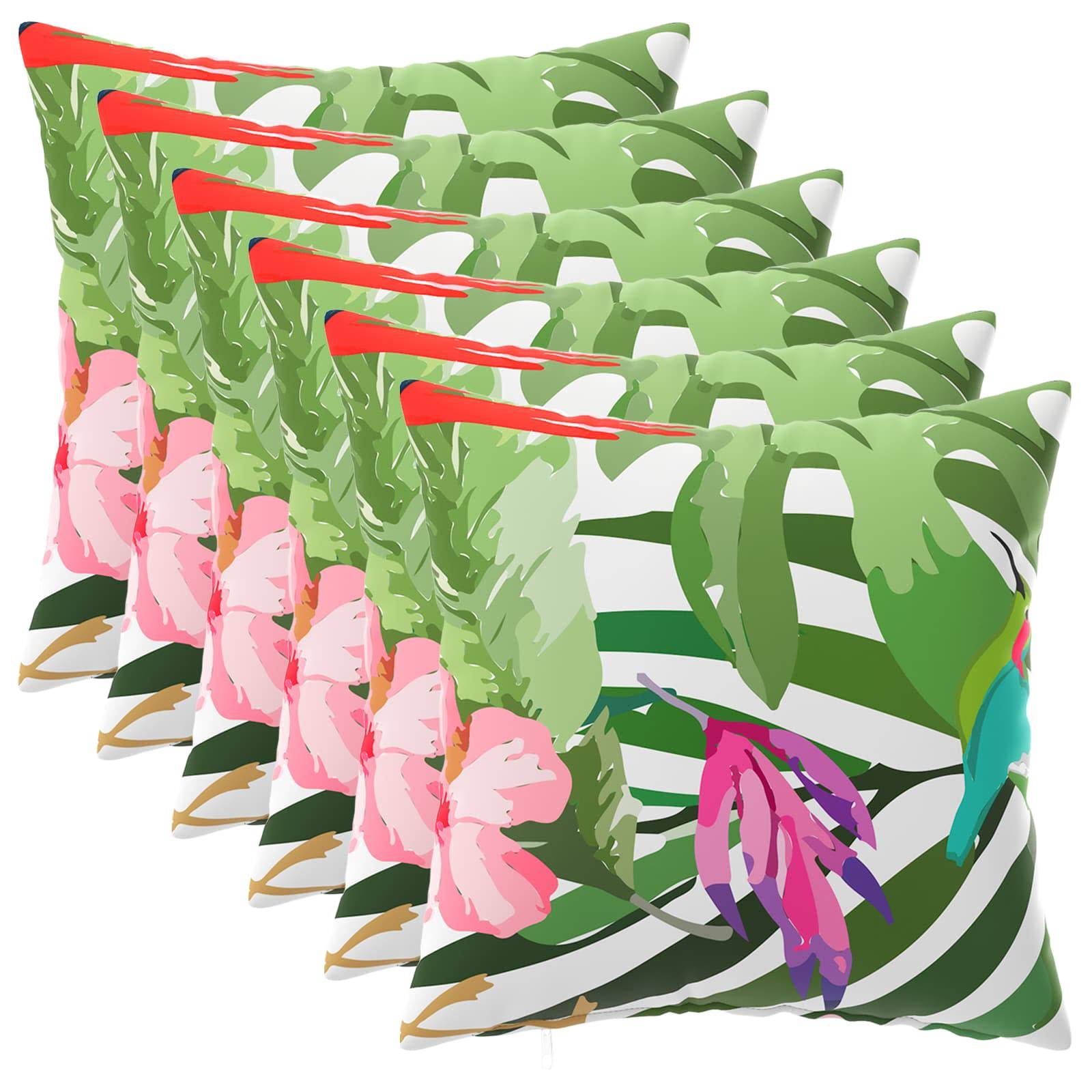 Stapel von Dekokissen mit Tropenprint, grüne Palmblätter und rosa Blüten in einer Reihe angeordnet.