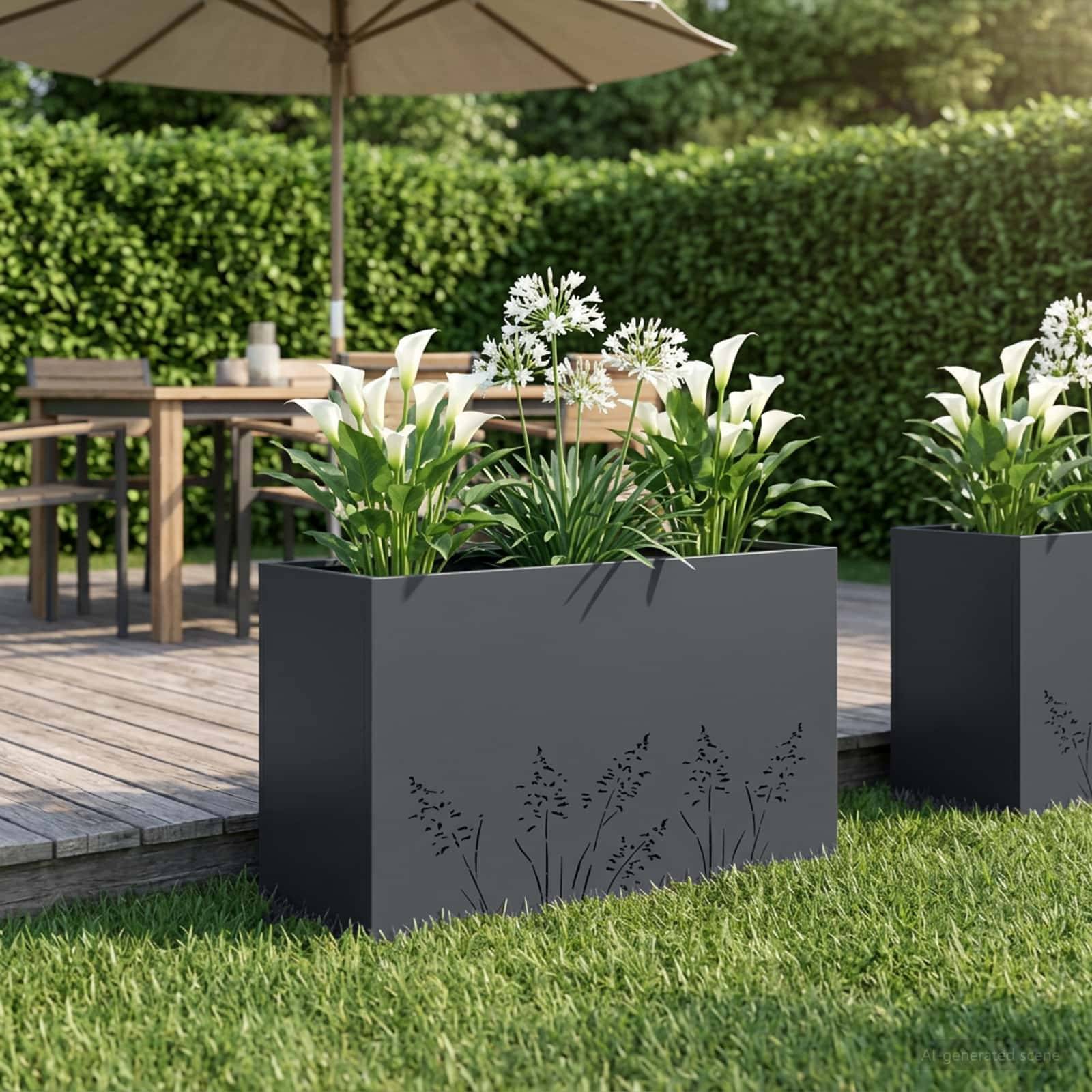 Außenterrasse mit zwei dunklen rechteckigen Pflanzkübeln mit weißen Lilien und Blattwerk neben einem Holztisch und Sonnenschirm auf einer Terrasse, mit Rasen und Heckenkulisse im Hintergrund.