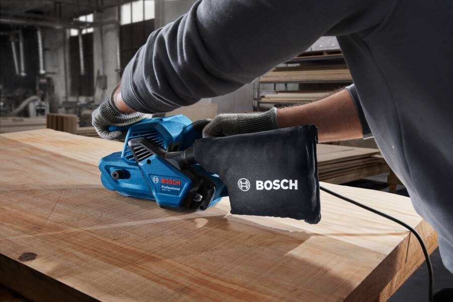 Arbeiter, der einen tragbaren elektrischen Bosch-Schleiffer auf einem Holzbrett in einer Werkstatt verwendet.