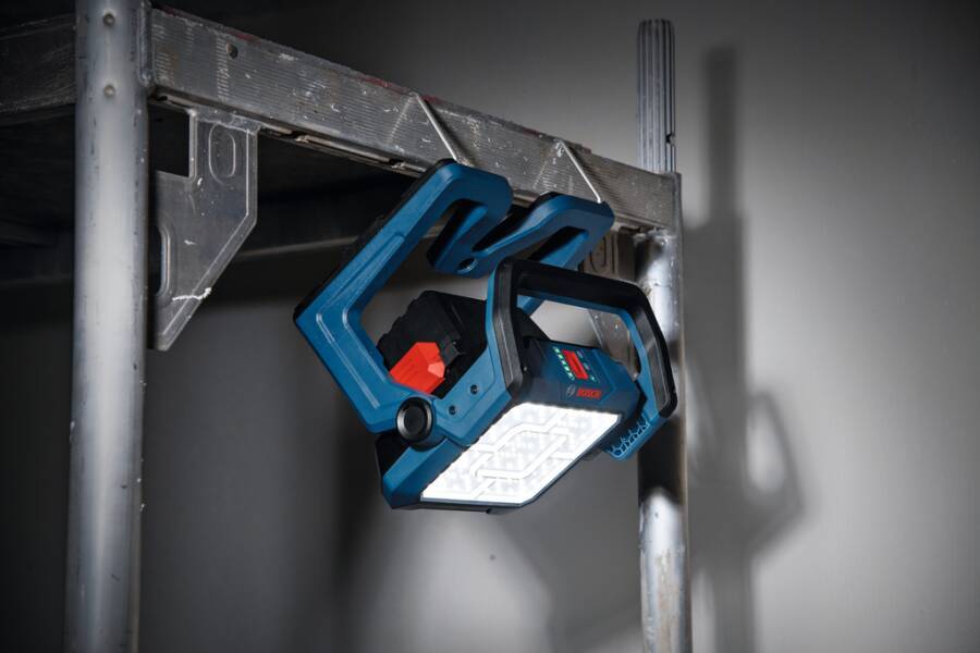 Tragbares blaues LED-Arbeitslicht, das von einem Metallgerüstrahmen hängt und den Bereich gegen eine graue Wand beleuchtet.