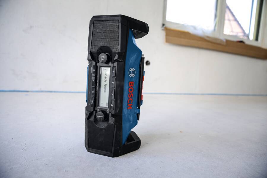 Ein tragbarer Radiomusiksprecher von Bosch steht aufrecht auf einem blanken Boden neben einer Wand und einem Fenster.