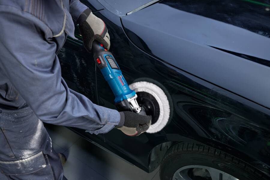Person poliert eine schwarze Autotür mit einem Elektroschleiffer, reinigt den Lack in der Nähe des Hinterrads