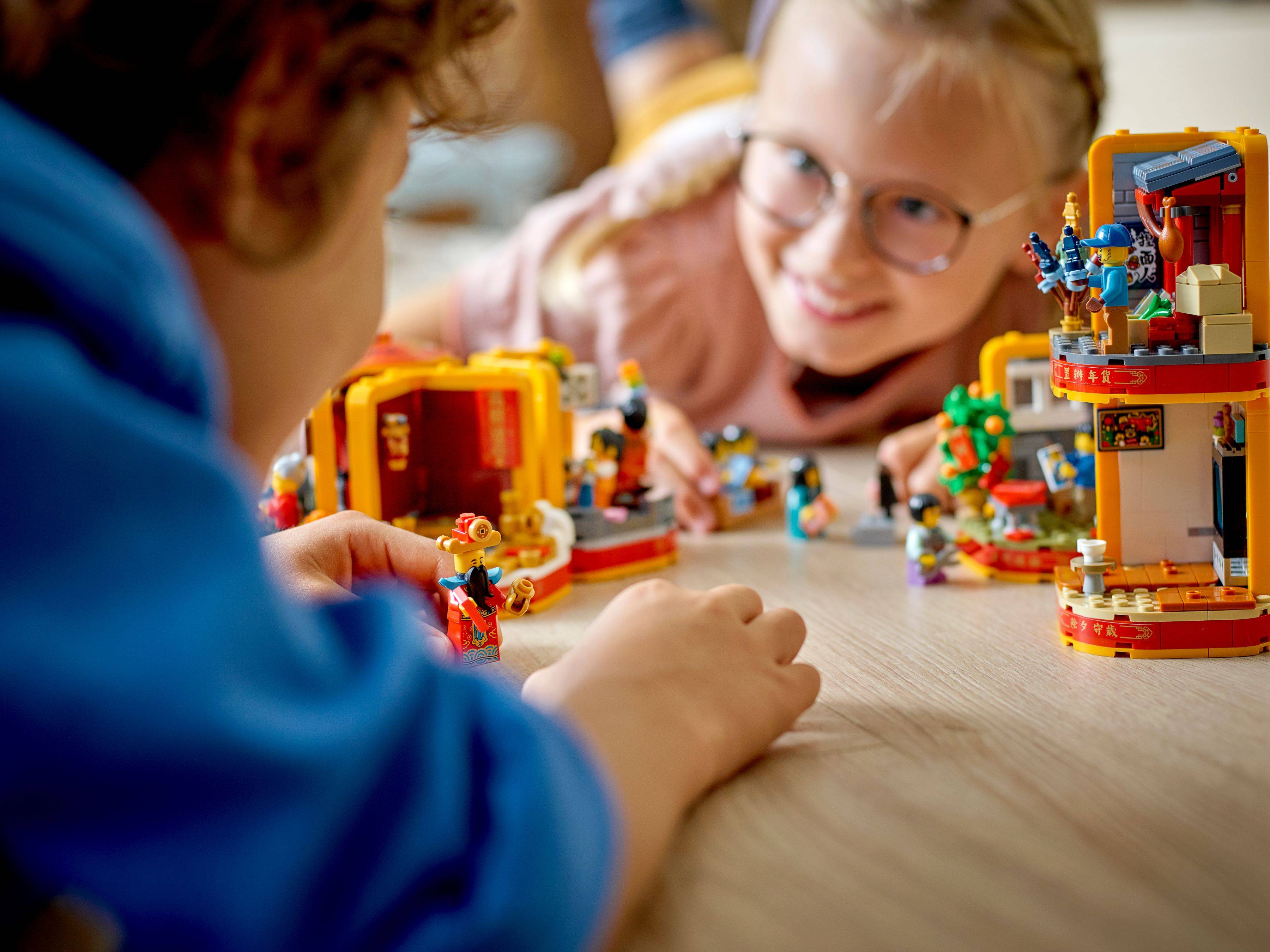 Kinder spielen zusammen mit einem farbenfrohen Spielzeug-Bauset auf einem Tisch, mit einem Jungen im Vordergrund und einem Mädchen, das im Hintergrund lächelt.