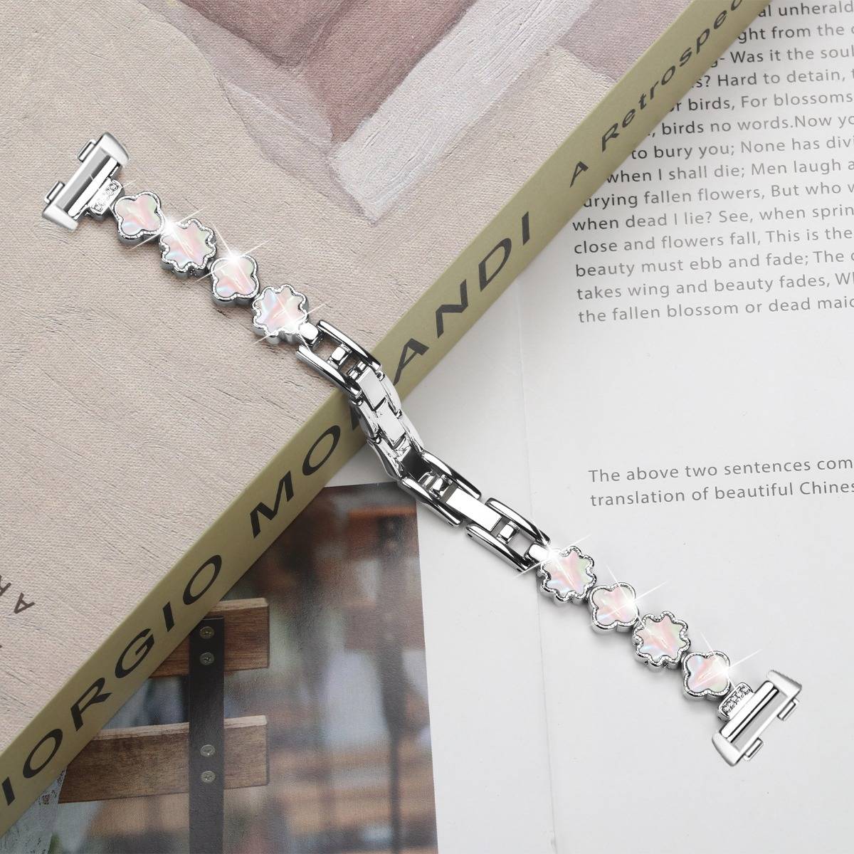 Silbernes Armband mit rosa blütenförmigen Gliedern, das über einer offenen Buch- oder Zeitschriftenseite drapiert ist.