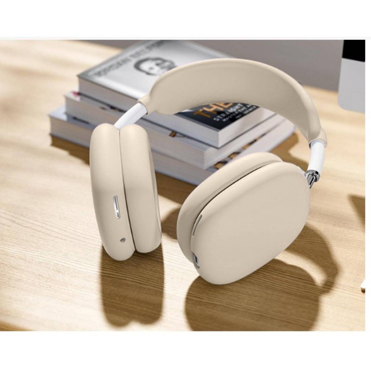 Beige Over-Ear-Kopfhörer mit kabelloser Verbindung, die auf einem Holzschreibtisch neben einem Stapel Bücher liegen.