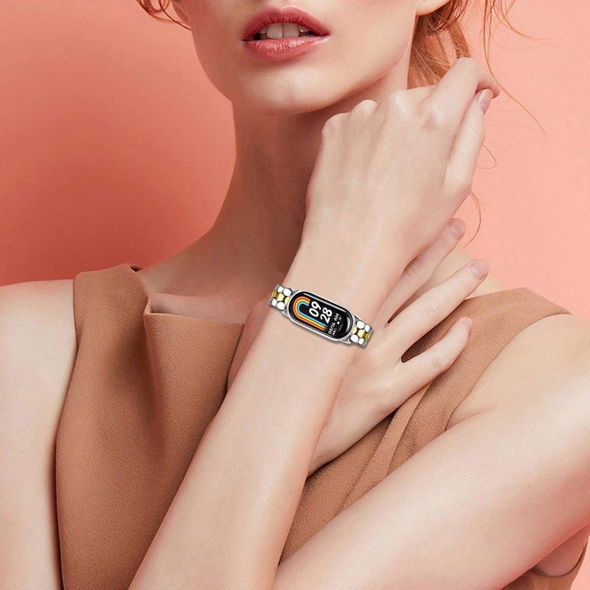 Nahaufnahme einer Frau, die ein schlankes Smart-Armband mit Farbdisplay am Handgelenk gegen einen rosa Hintergrund trägt.