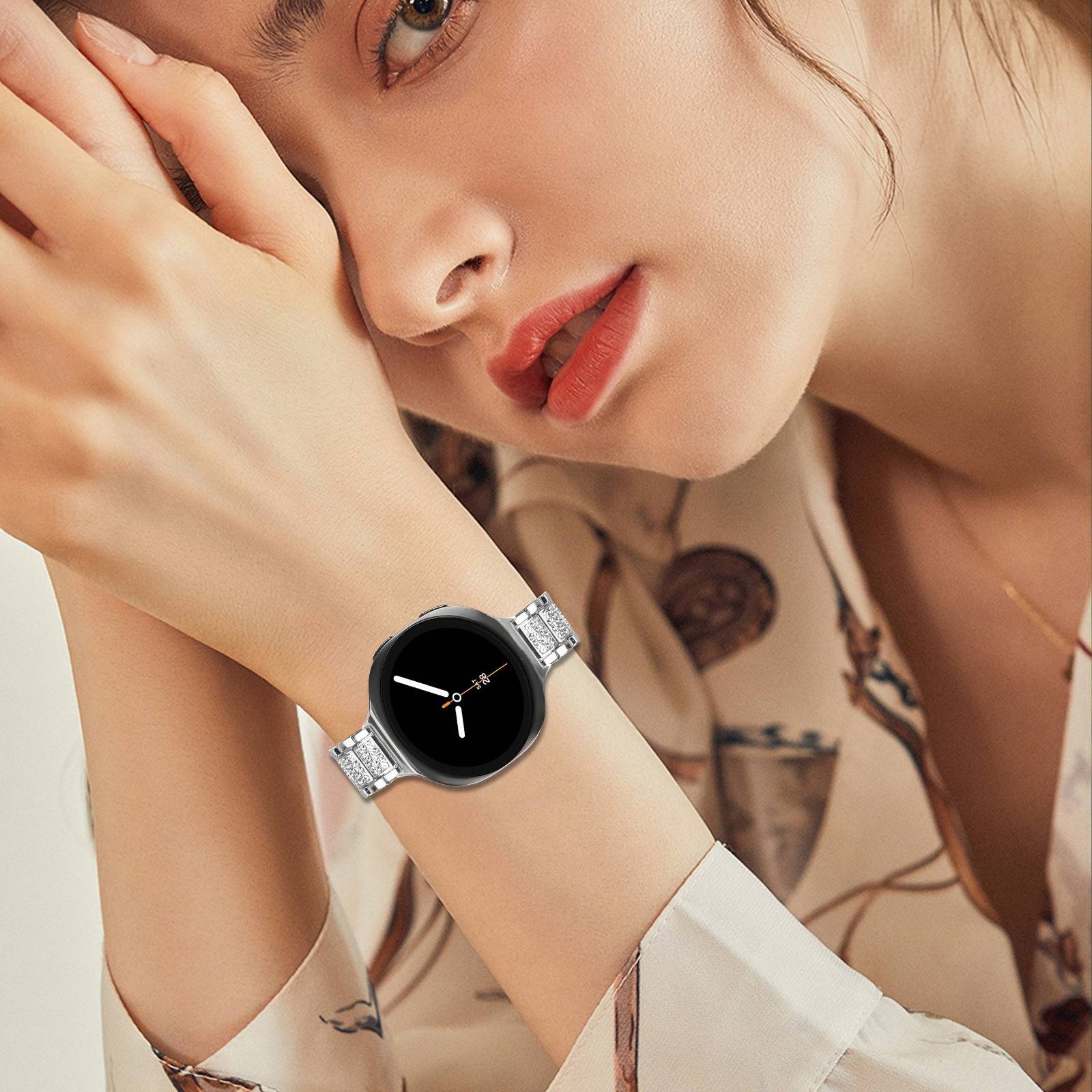 Nahaufnahme einer Frau, die mit ihrer Hand in der Nähe ihres Gesichts posiert und eine silberne Smartwatch mit rundem schwarzem Display trägt.