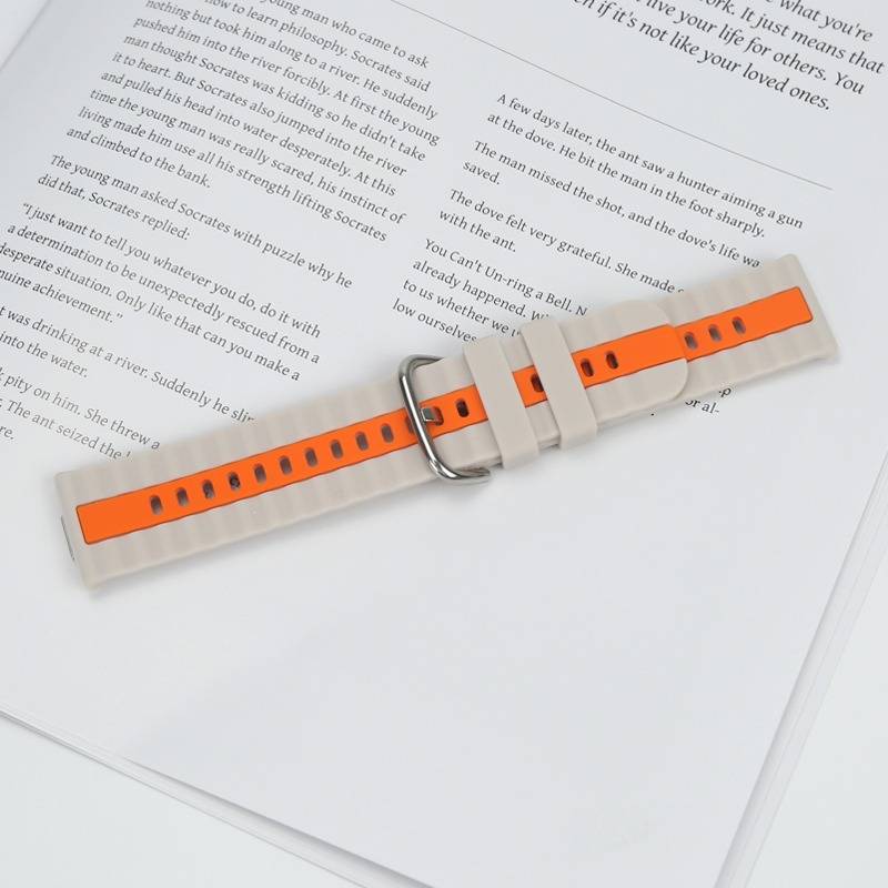 Orange-weiß gestreiftes Smartwatch-Armband mit silberner Schnalle liegt auf einer offenen Buchseite, was eine Produktpräsentation suggeriert.