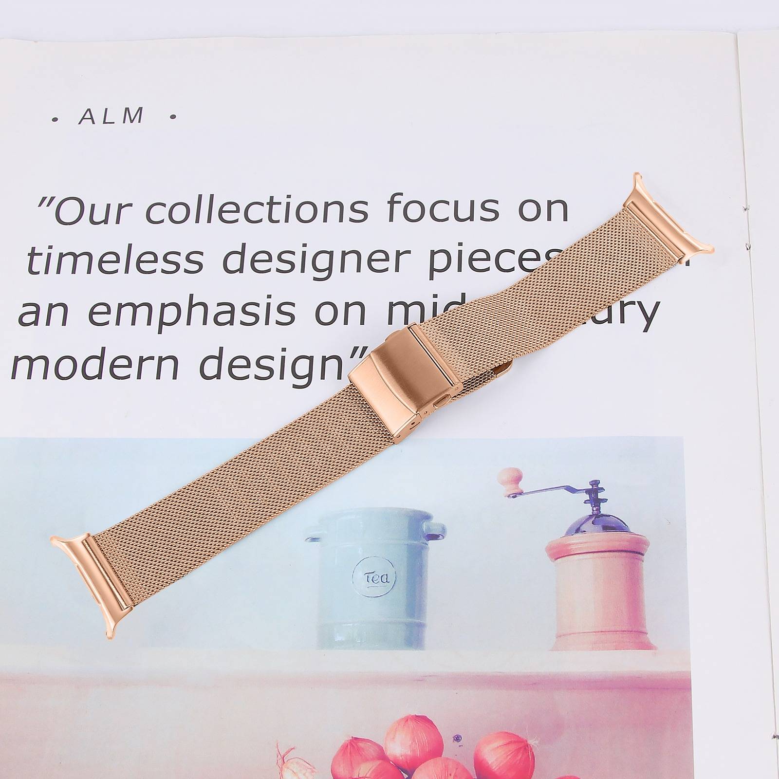 Rosegoldfarbenes Mesh-Uhrenarmband diagonal über einer Magazinseite gelegt mit dem Zitat „Unsere Kollektionen konzentrieren sich auf zeitlose Designer-Stücke... modernes Design".