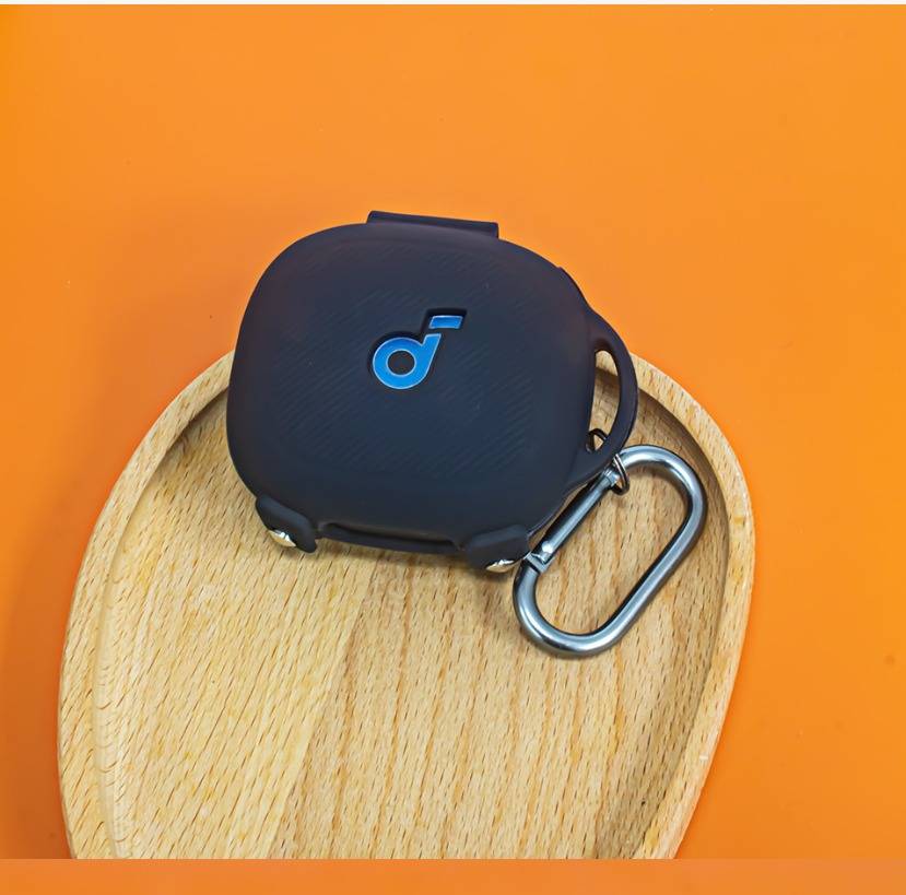 Schwarze Ohrhörer mit Ladeetui mit blauem Logo und Karabinerhaken, ruhend auf einem kleinen Holztablett vor orangefarbenem Hintergrund.
