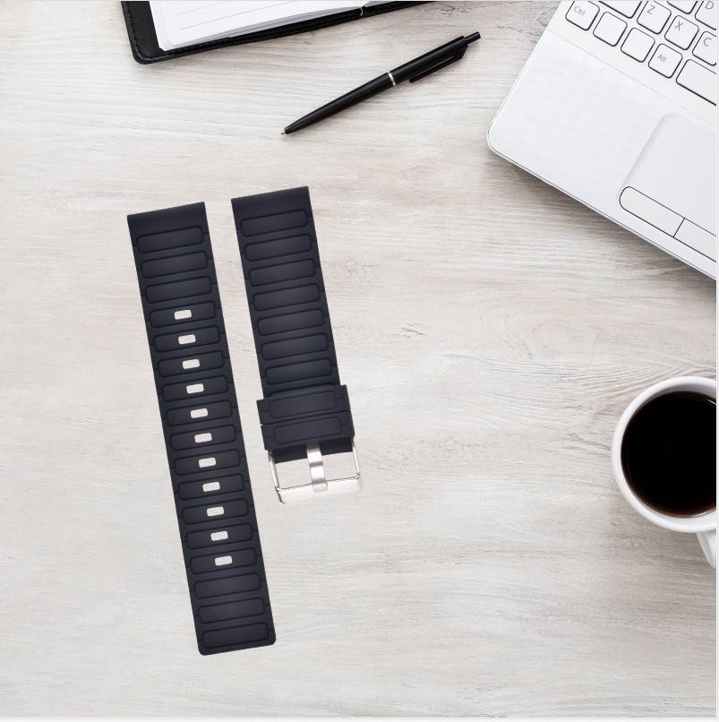 Zwei schwarze Uhrenarmbänder liegen auf einem hellen Schreibtisch neben einem Laptop, Stift, Notizbuch und einer Tasse Kaffee.