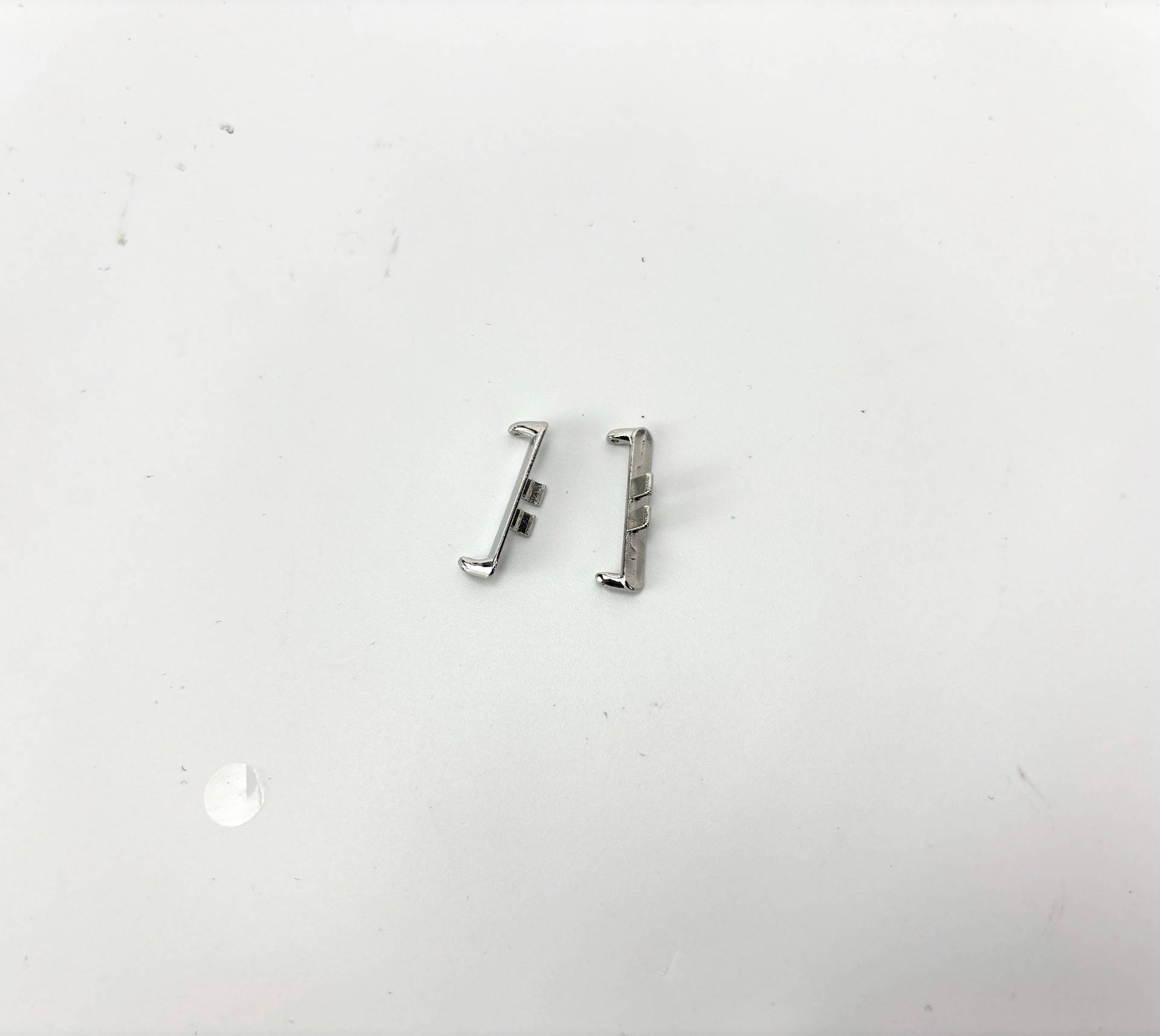 Zwei kleine silberne Metallscharniere oder Verschlussteile liegen nebeneinander auf einer weißen Oberfläche.