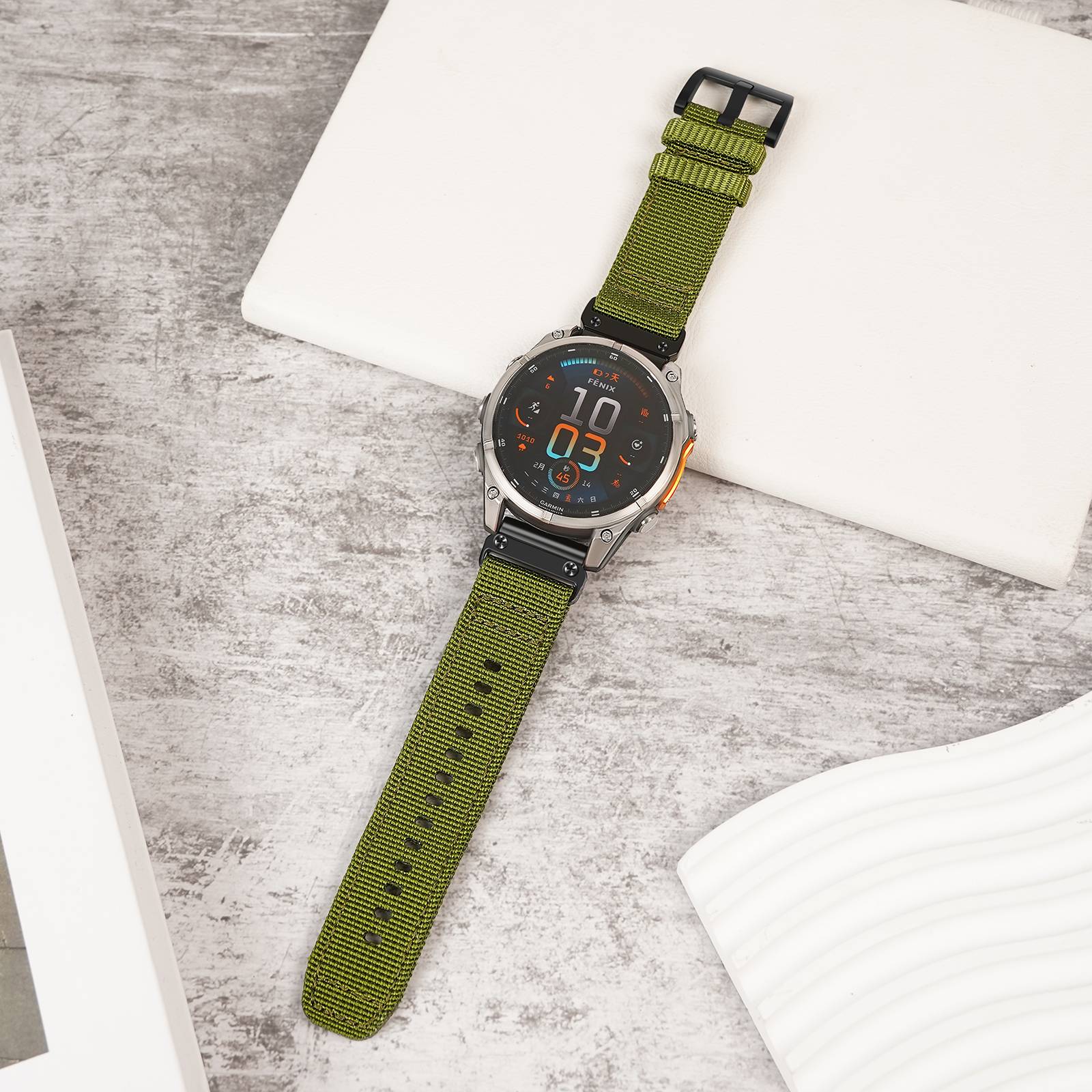 Grüne-Riemen-Smartwatch mit rundem digitalen Display auf einer weiß-grauen Tischplatte, gezeigt in einer flach ausgelegten Produktfoto-Stilaufnahme.