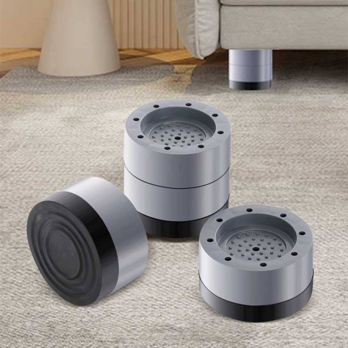 Drei silberne zylindrische Möbelfüße oder Vibrationsdämpfer auf einem Teppichboden, einer liegt auf der Seite und zwei stehen aufrecht neben einem Sofa.