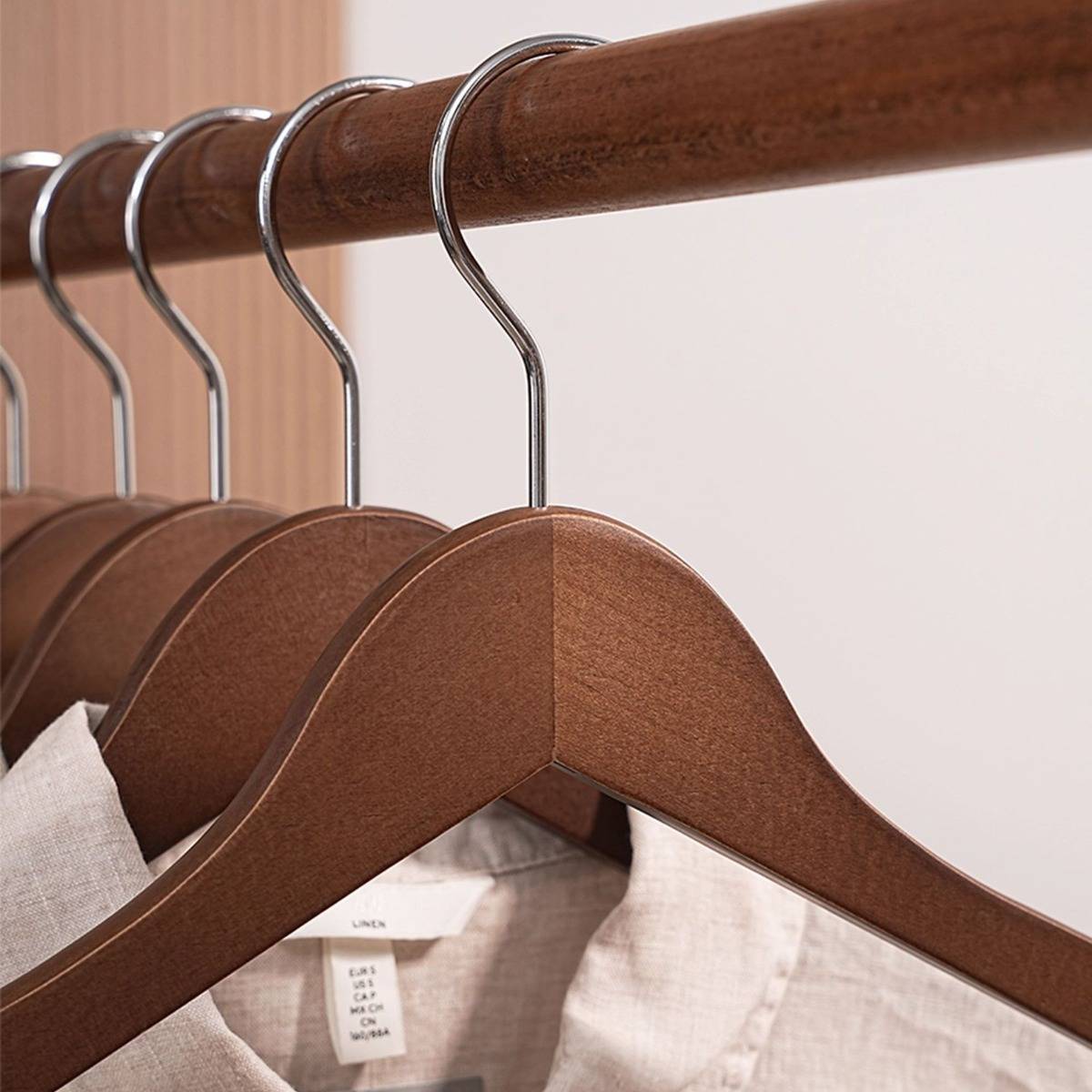 Nahaufnahme von Holzkleiderbügeln, die hellfarbige Hemden auf einem Kleiderständer halten.