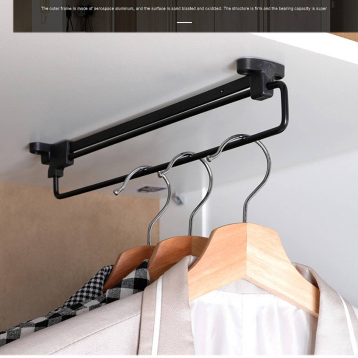 Schwarzes wandmontiertes Kleiderschrank-Gestell mit drei Holzbügeln, an denen Kleidung hängt, angebracht an einer Decke oder Wand in der Nähe eines Kleiderschranks.
