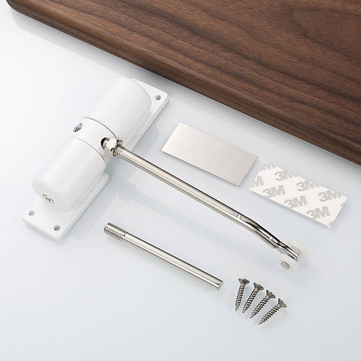 Weiß Türscharnier-Set mit Metallarm, Montageplatte, Klebepads und Schrauben auf einer weißen Oberfläche neben einer Holzplatte