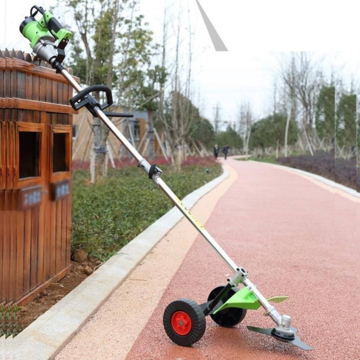 Grüner elektrischer Fadentrimmer mit Rädern, der an einem hölzernen Mülleimer neben einem gewundenen Parkweg lehnt