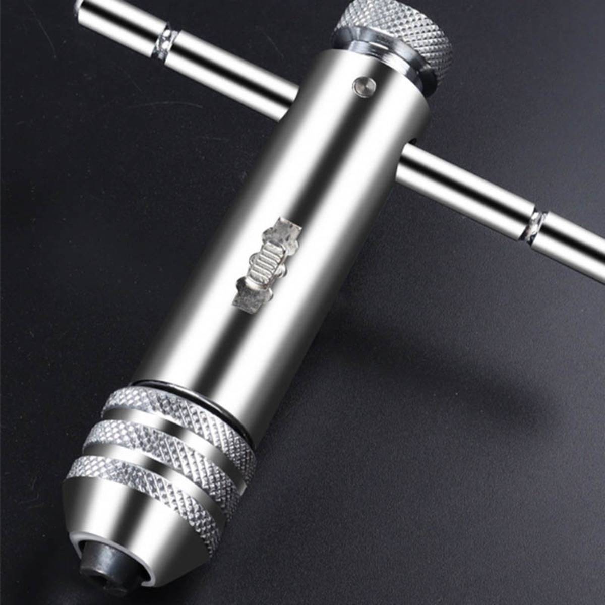 Nahaufnahme eines silbernen Metallhandwerkzeugs mit T-förmigem Griff und strukturierter Grifffläche, dargestellt auf dunklem Hintergrund.