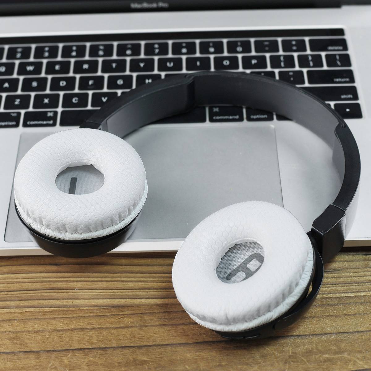 Schwarze Over-Ear-Kopfhörer mit weißen Ohrpolstern ruhen auf einer Laptop-Tastatur und einem Trackpad auf einem Holzschreibtisch.