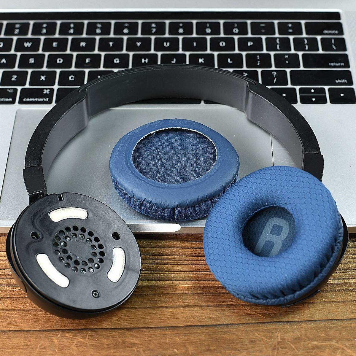 Drei blau-schwarze Kopfhörer-Ohrpolster und ein schwarzes Kopfband liegen auf einer Laptop-Tastatur und einem Schreibtisch.