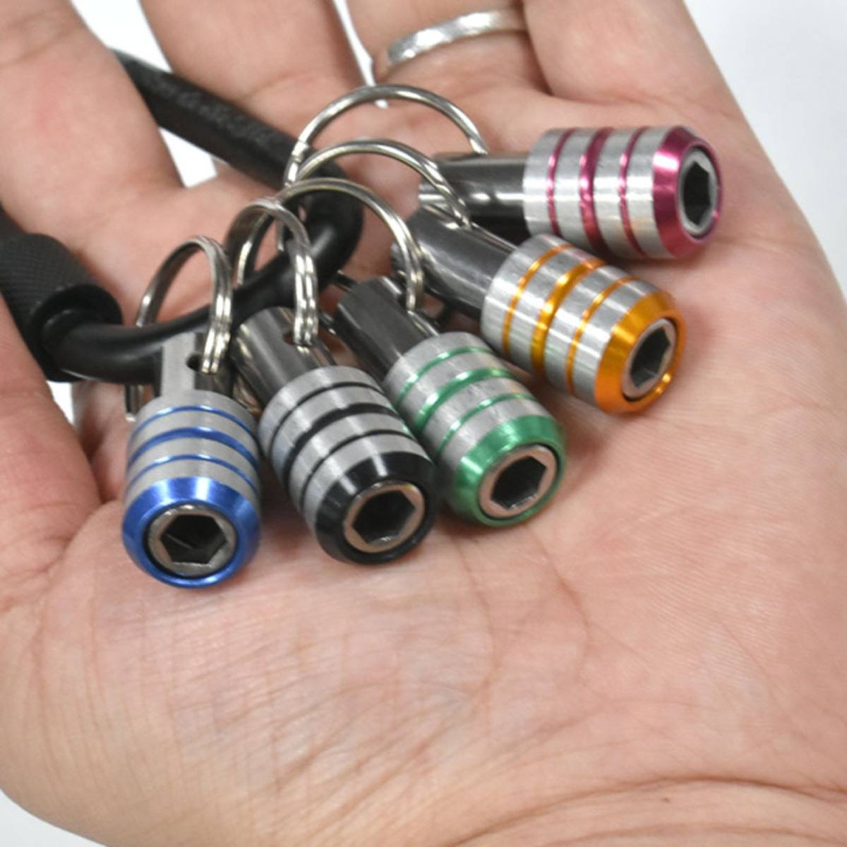 Hand, die fünf kleine farbcodierte Kabelschlösser mit Metallschleifen und sechseckigen Öffnungen hält, jeweils mit Tags versehen, um verbundene Kabel zu identifizieren.
