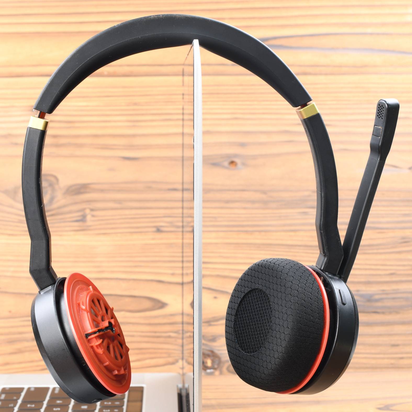 Schwarze Over-Ear-Kopfhörer, die auf beiden Seiten eines Computermonitors gezeigt werden, wobei ein Ohrkissen freigelegt ist, um den Treiber und rote innere Komponenten zu enthüllen.