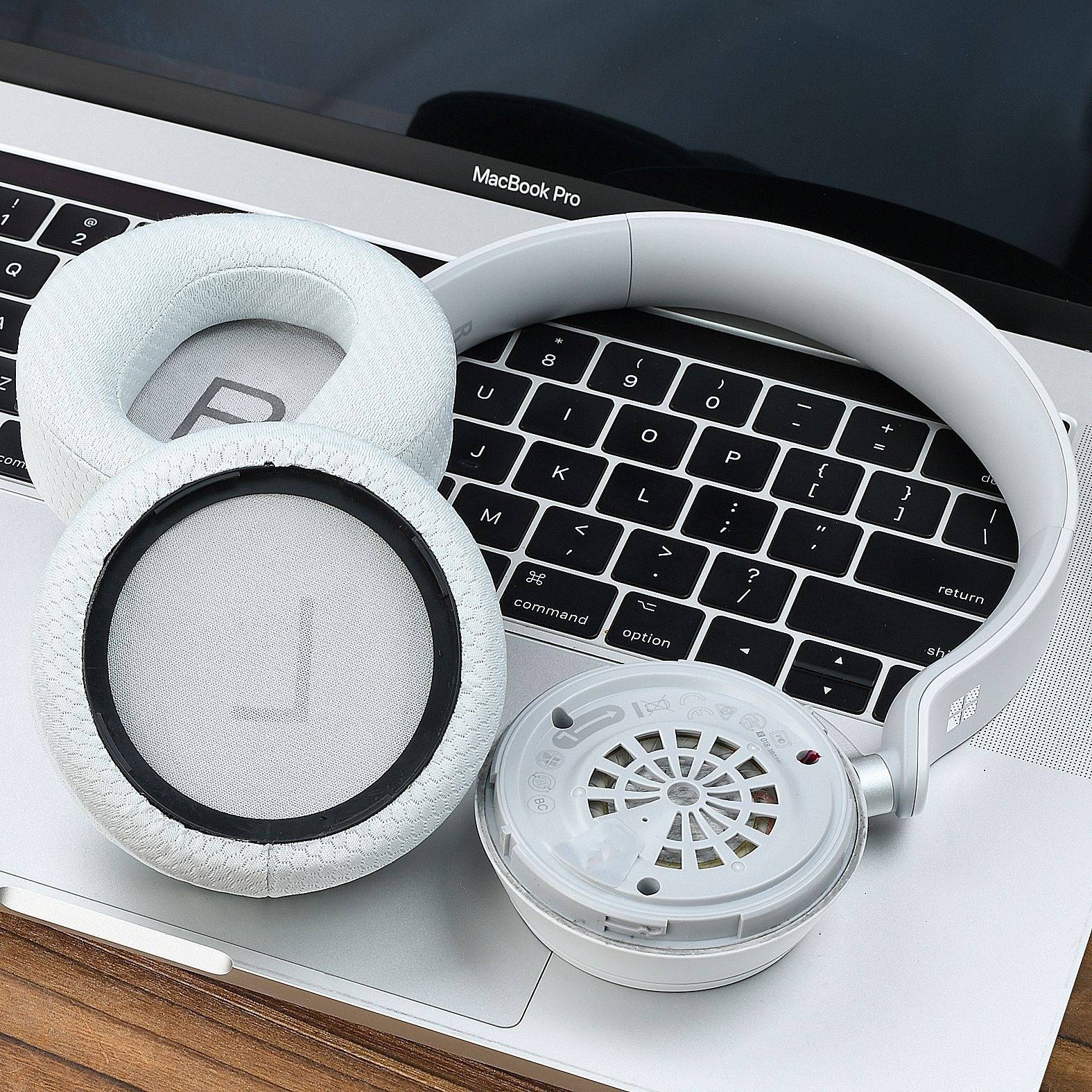 Weiße Over-Ear-Kopfhörer mit Schaumstoff-Ohrpolstern ruhen auf einer MacBook-Pro-Tastatur, wobei eine Ohrmuschel die innere Lautsprecherseite zeigt.