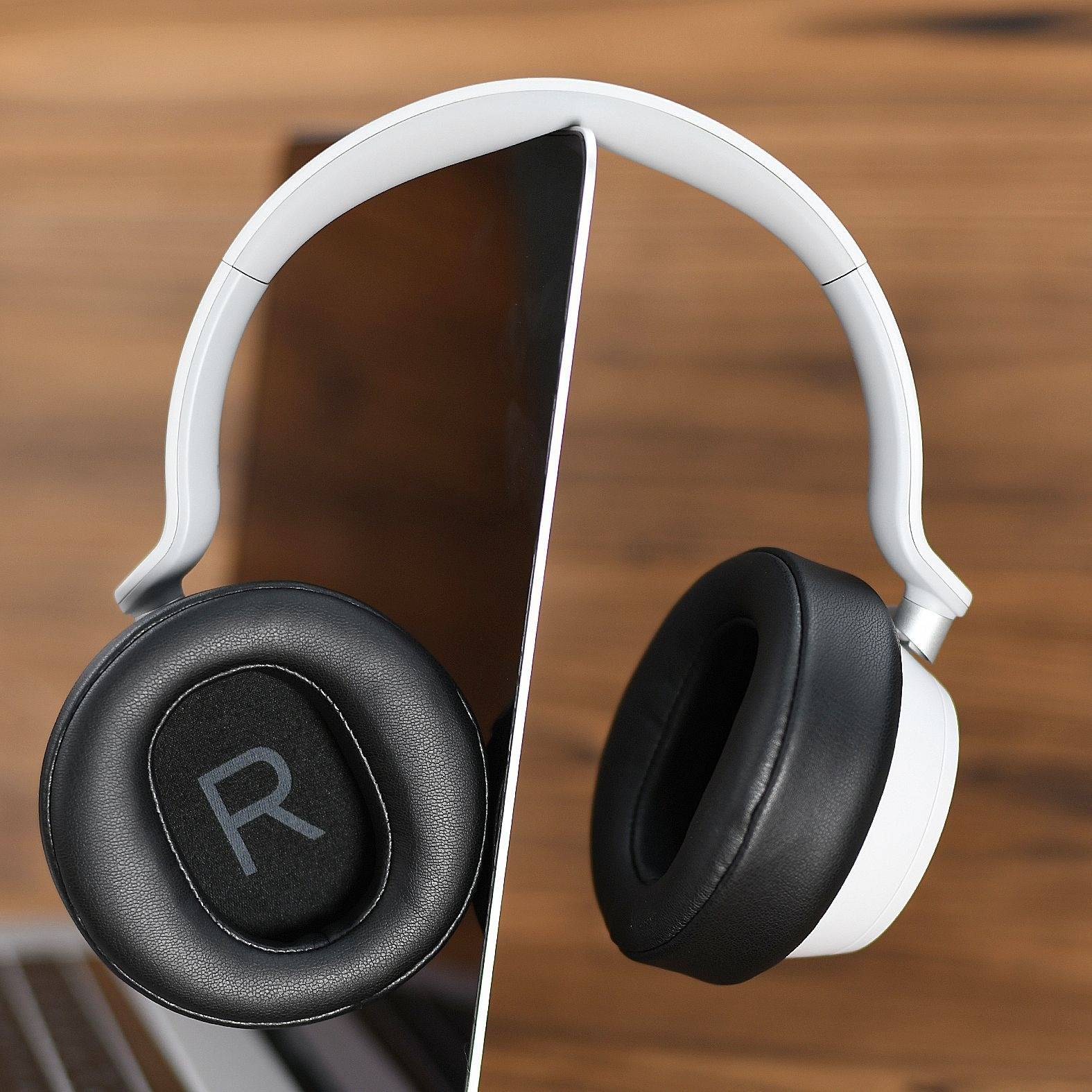 Weiße Over-Ear-Kopfhörer mit schwarzen Ohrpolstern, in der Mitte aufgeteilt dargestellt, um das innere Design zu zeigen, auf einer Holzoberfläche.