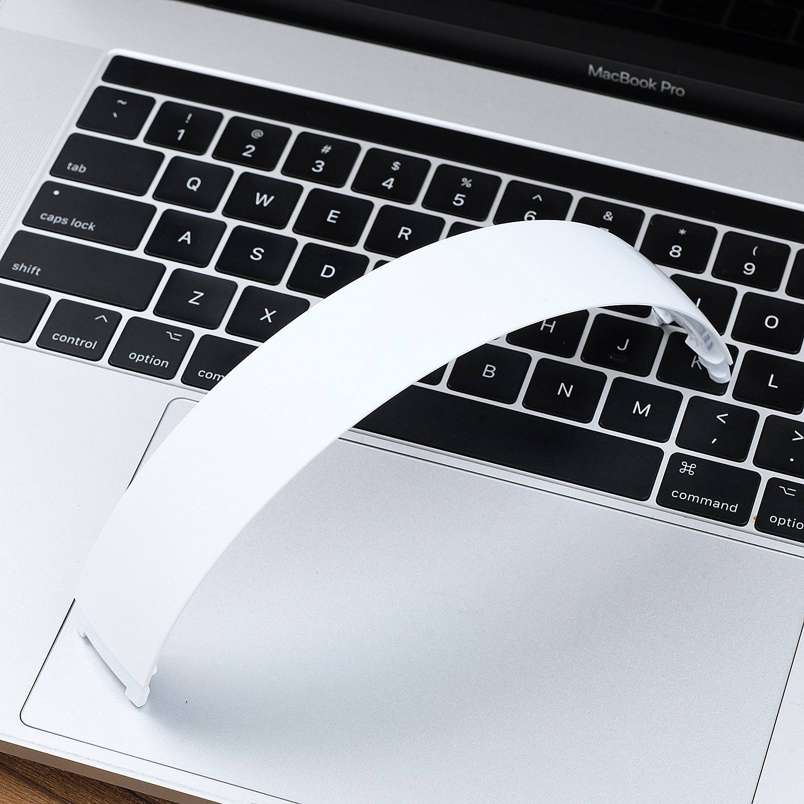 Ein weißer Papierstreifen wölbt sich über eine MacBook Pro-Tastatur und ein Trackpad, wobei er die Tasten teilweise bedeckt.