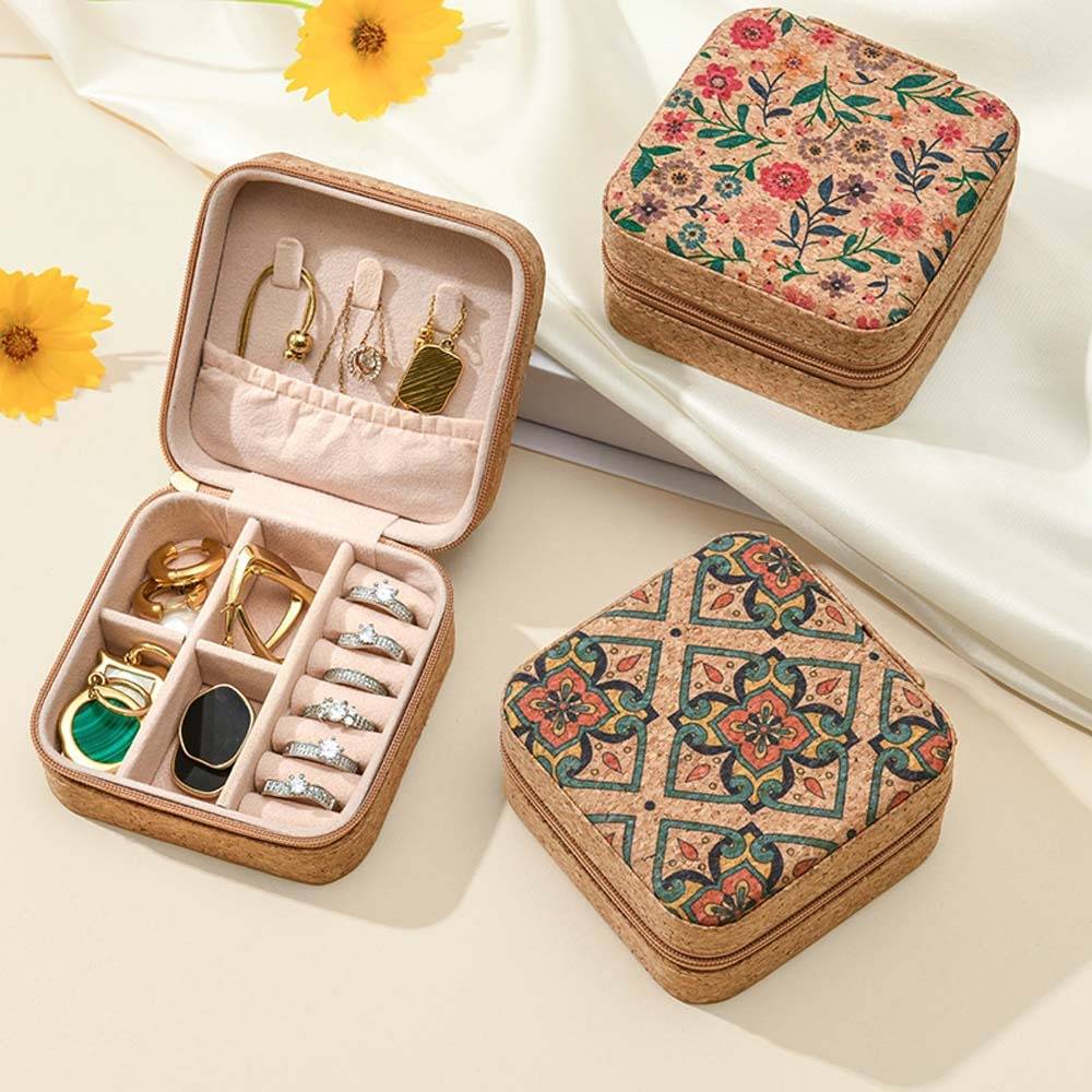 Drei Schmuckkästchen mit Blumenmuster, eines offen mit Ringen, Ohrringen und Armbändern, die in gepolsterten Fächern organisiert sind, auf einer hellen Stoffoberfläche mit gelben Blüten.